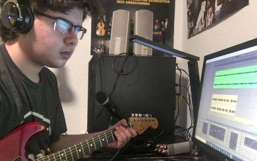 A MUSICIAN AT HIS NATURAL HABITAT: Junior Adam Bauer gently strokes a harmonious chord on his guitar, which is plugged into an interface that transfers the music to his digital audio workstation.