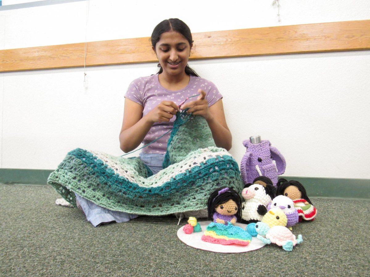 THE ART OF CROCHET: Junior Shriya Balaji works on her latest project, a green blanket, while sitting beside some of her other works, including a crocheted portrait of herself. 