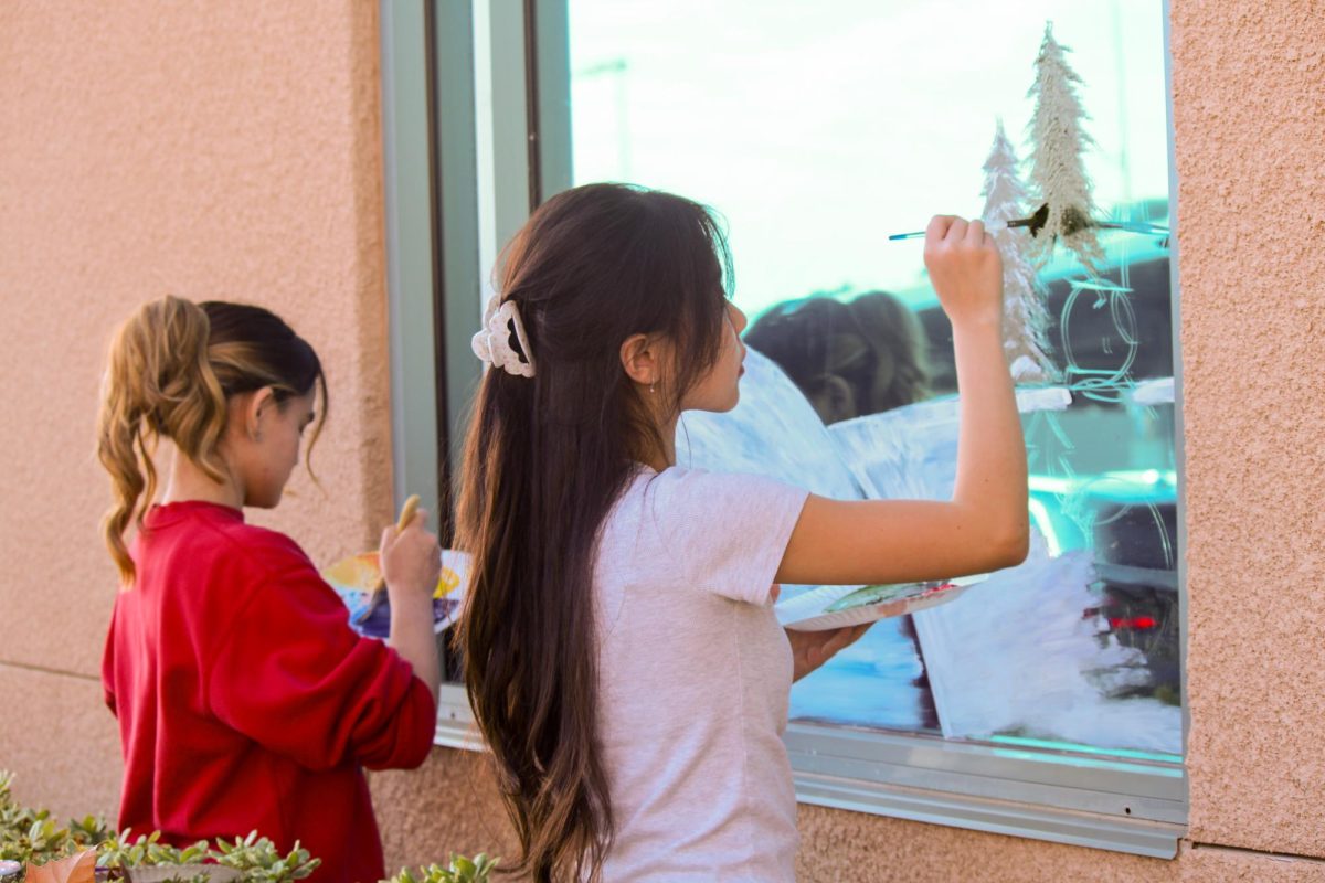 WINTER WISHES: Seniors Belle Bolin and Angelina Guo decorate the front office windows in preparation for the holidays.